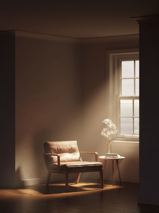 An empty chair in warm light beside a window with flowers
